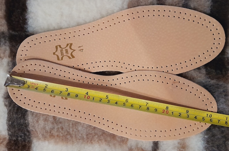 May include: Two brown leather insoles with a perforated pattern. The insoles are measured with a yellow tape measure, showing a length of 10 inches. The insoles are labeled "BONTES UBER" and "41".