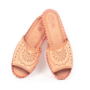 Puede incluir: Un par de sandalias de cuero marrón con costuras rojas y un diseño floral. Las sandalias tienen la punta abierta y una suela plana.