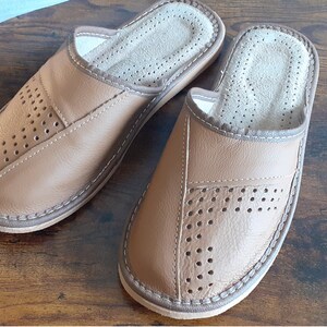 Op de afbeelding: Een paar bruine leren slippers met een geperforeerd ontwerp. De slippers hebben een gesloten neus en een slip-on stijl.
