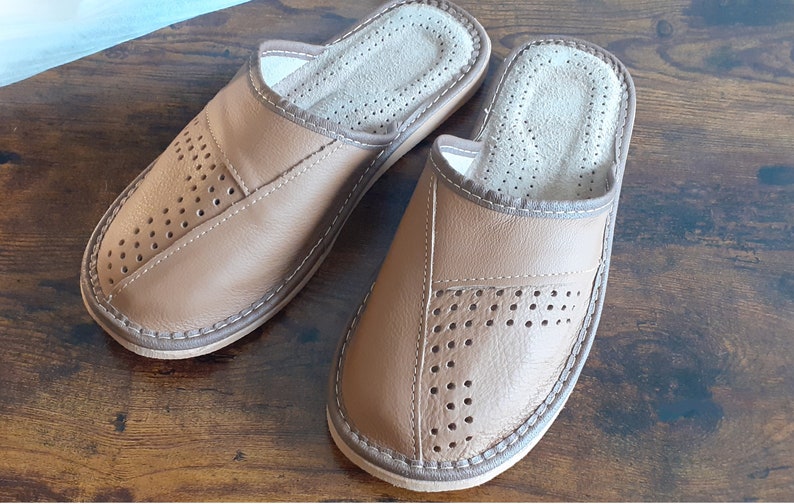 Op de afbeelding: Een paar bruine leren slippers met een geperforeerd ontwerp. De slippers hebben een gesloten neus en een slip-on stijl.