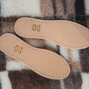 May include: Two brown leather insoles with a stitched edge and a small brown leather label that says "Genuine Leather" on a brown and white plaid fabric background.