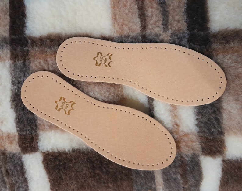 May include: Two brown leather insoles with a stitched edge and a small brown leather label that says "Genuine Leather" on a brown and white plaid fabric background.