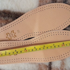 May include: Two pairs of beige leather insoles with a perforated design. The insoles are measured with a tape measure, showing a length of 10 inches.