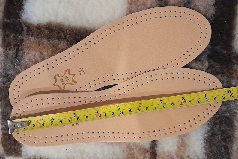 May include: Two pairs of beige leather insoles with a perforated design. The insoles are measured with a tape measure, showing a length of 10 inches.