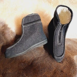 May include: A pair of gray felt boots with white stitching and a zipper closure. The boots have a soft, white interior lining and a dark gray sole. The boots are designed for warmth and comfort.