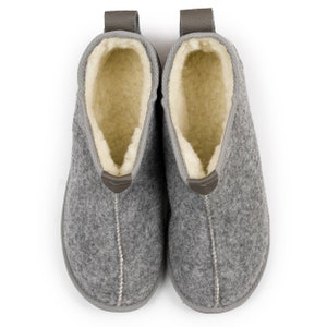 May include: A pair of gray wool slippers with a brown leather pull tab and a white fleece lining.