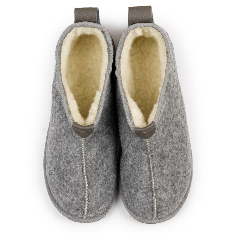 May include: A pair of gray wool slippers with a brown leather pull tab and a white fleece lining.