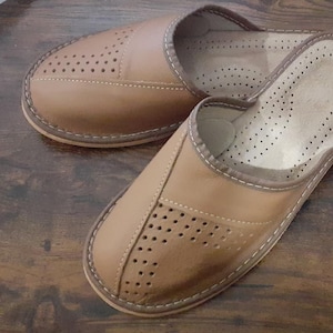 Op de afbeelding: Een paar bruine leren slippers met een geperforeerd ontwerp. De slippers hebben een gesloten neus en een slip-on stijl.