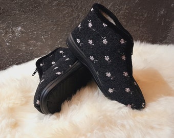 May include: A pair of black fuzzy slippers with a white floral pattern. The slippers have a closed toe and a zipper on the side.