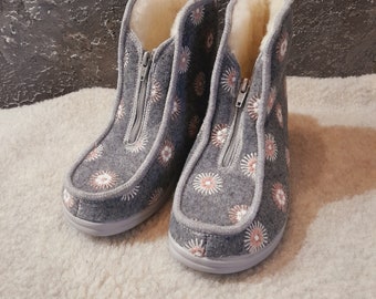 Puede incluir: Un par de zapatillas de fieltro gris con una cremallera en la parte delantera. Las zapatillas tienen un patrón floral bordado.