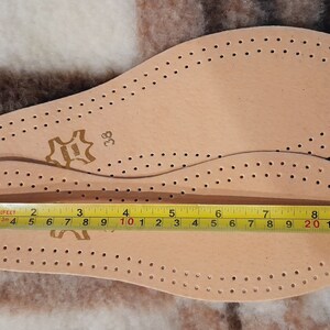 May include: Two beige leather insoles with a perforated pattern. The insoles are sized 38 and measure 10 inches in length.