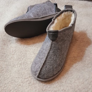 May include: A pair of gray felt slippers with black leather accents and a white fleece lining. The slippers have a simple, comfortable design.