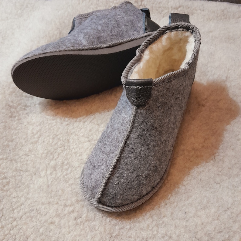 May include: A pair of gray felt slippers with black leather accents and a white fleece lining. The slippers have a simple, comfortable design.