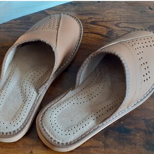 Op de afbeelding: Een paar lichtbruine leren slippers met een geperforeerd ontwerp. De slippers hebben een gesloten neus en een slip-on stijl.
