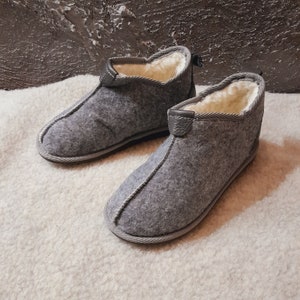 May include: A pair of gray felt slippers with a white fleece lining. The slippers have a simple, rounded toe and a closed back.