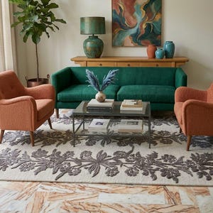 May include: A living room arrangement featuring a deep green sofa flanked by two textured orange armchairs. A glass-topped coffee table sits on a cream-coloured area rug with a dark grey floral pattern. A wooden console table holds a lamp and vases.