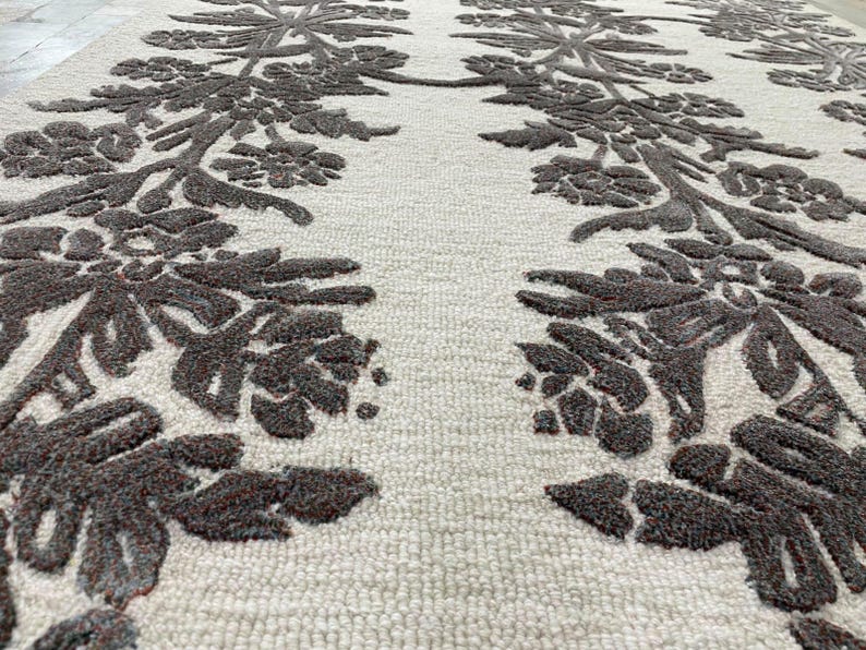 May include: A rectangular area rug featuring a cream-coloured base with a raised, dark brown floral pattern. The design consists of two vertical columns of symmetrical, textured botanical motifs that run the length of the rug surface.