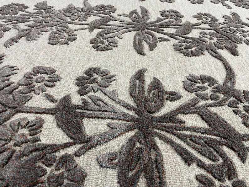 May include: A textured area rug featuring a light beige background with a raised, dark brown floral pattern. The design consists of interconnected flowers, leaves, and stems that create a dense, repeating botanical motif across the surface.