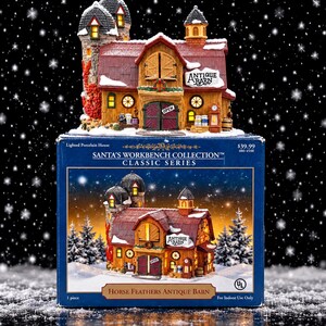 May include: A porcelain lighted miniature barn from the Santa's Workbench Collection, featuring a red roof, stone tower, and snow-dusted exterior. The building has a sign reading Antique Barn, a green door with an Open sign, and warm interior lighting.
