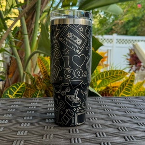 May include: A black stainless steel tumbler with a white design featuring 80s icons like cassette tapes, a joystick, and the text "I love 80s".