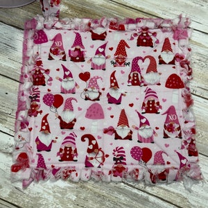 May include: Pink and red quilted pot holder with a Valentine's Day gnome theme. The pot holder has a frayed edge and a hanging loop.