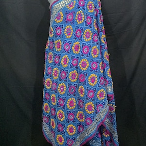 Könnte beinhalten: Blauer Stoff mit einem Blumenmuster in Pink und Gelb, akzentuiert mit kleinen Spiegeln. Der Stoff ist über einer Schaufensterpuppe drapiert, was das komplizierte Design und die Bordürendetails zeigt. Der Stoff hat einen rosa Rand.