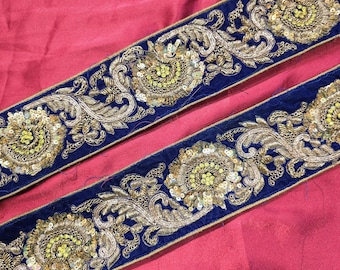 May include: Two strips of ornate blue fabric with gold embroidery and sequins. The design features floral and scroll patterns. The fabric is set against a pink background, creating a striking contrast.