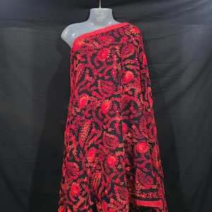 Könnte beinhalten: Schwarzer Stoff mit aufwendiger roter Blumenstickerei. Der Stoff ist über eine Schaufensterpuppe drapiert und zeigt das detaillierte Muster. Die Kanten sind mit einem roten Rand versehen, der das Design hervorhebt.