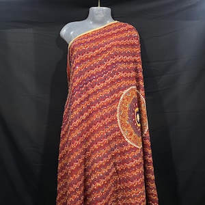Könnte beinhalten: Ein weinroter Stoff mit Zickzackmuster und einem großen kreisförmigen Design. Der Stoff ist über eine Schaufensterpuppe drapiert. Das kreisförmige Design weist ein detailliertes Muster mit Orange-, Gelb- und Lilatönen auf.