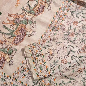 Może przedstawiać: Kremowy materiał z misternym haftem. Wzór przedstawia słonie i motywy kwiatowe w odcieniach zieleni, pomarańczy i fioletu. Krawędzie są obramowane szczegółowym wzorem ściegu. Ten materiał to prawdopodobnie przedmiot dekoracyjny lub tkanina.