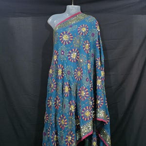 Könnte beinhalten: Türkisfarbener Stoff mit gestickten Blumenmustern und Pailletten-Akzenten. Der Stoff ist über eine Schaufensterpuppe drapiert und zeigt das komplizierte Design. Die Kanten sind mit einem rosa Rand versehen.