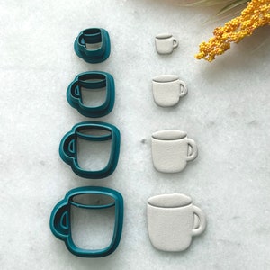 Pode incluir: Conjunto de seis cortadores de biscoitos de plástico azul-esverdeado e branco em forma de canecas de diferentes tamanhos.