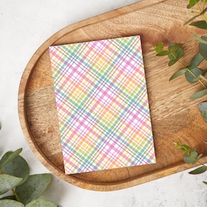 Pode incluir: Um cartão branco com um padrão xadrez colorido em tons de rosa, amarelo, verde e azul. O cartão está em uma bandeja de madeira.