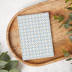 May include: A white card with a repeating pattern of blue and gold geometric shapes. The card is on a wooden tray.