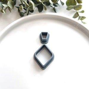 May include: Two gray plastic cookie cutters, one shaped like a diamond and the other shaped like a pointed oval, on a white surface.