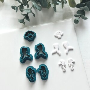 May include: A set of teal and white plastic cookie cutters in the shape of seashells, mermaids, and seahorses.