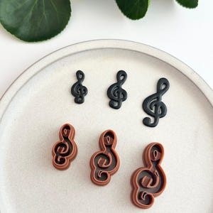 May include: Five treble clef cookie cutters in different sizes. Two are black and three are brown.