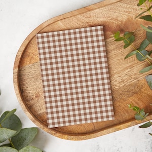 May include: A brown and white gingham patterned card on a wooden tray with green leaves.
