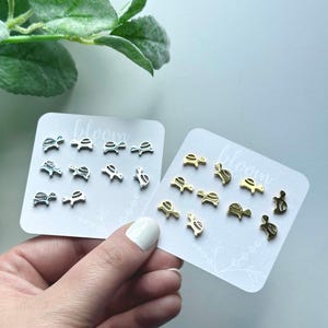 May include: Two cards with the word "bloom" printed on them. Each card has a set of small turtle earrings. One set is silver and the other is gold.