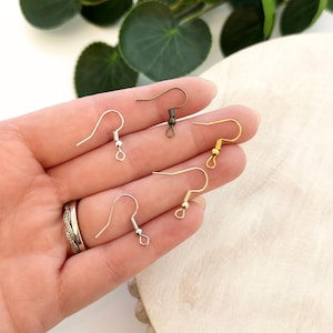 May include: A collection of earring hooks in various metallic finishes, including silver, gold, and bronze. The hooks are displayed against a neutral background, showcasing their different styles and colors. The hooks are designed for jewelry making.