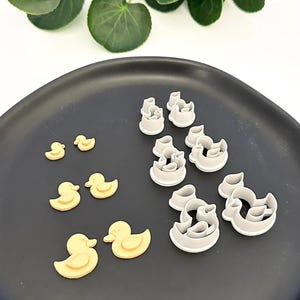 Może przedstawiać: Zestaw 10 foremek do ciasteczek w kształcie kaczek. Formy są wykonane z plastiku i są w dwóch kolorach: żółtym i szarym. Formy są ułożone na czarnym talerzu.