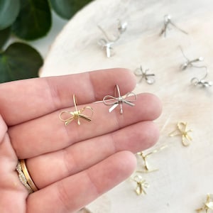 Pode incluir: Um par de brincos de laço, um dourado e outro prateado. Os brincos são pequenos e delicados, perfeitos para adicionar um toque de elegância a qualquer roupa.