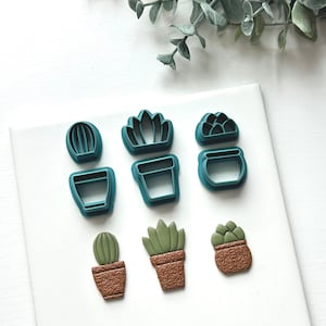 May include: Set of six teal green plastic cookie cutters shaped like potted succulents and cacti. The cutters are arranged on a white surface.