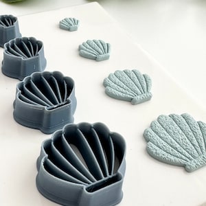 May include: A set of six blue and light blue plastic seashell cookie cutters. The cutters are arranged in a row from smallest to largest.