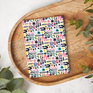 Pode incluir: Um cartão branco com um padrão repetitivo de formas abstratas coloridas, incluindo círculos, quadrados, linhas onduladas e arcos. As formas são em tons de rosa, azul, verde, amarelo e preto.