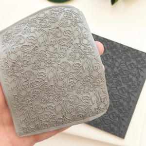 Pode incluir: Um molde de silicone cinza com um padrão repetido de personagens e símbolos de Star Wars. O molde é segurado em uma mão, com um segundo molde cinza mais escuro visível ao fundo. Os moldes estão em uma superfície branca.