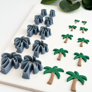 Puede incluir: Un conjunto de 10 cortadores de galletas de plástico gris en forma de palmera y 7 decoraciones de fondant de palmera verde y marrón.