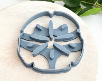 Könnte beinhalten: Ein grauer Plastik-Ausstecher in Form einer Sanddollar. Der Ausstecher hat ein detailliertes Design mit einem Sternmuster in der Mitte.