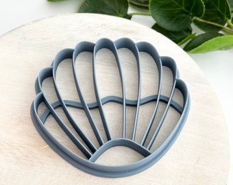 Könnte beinhalten: Ein grauer Plastik-Ausstecher in Form einer Muschel. Der Ausstecher ist muschelförmig mit einem gewellten Rand und einem erhabenen Design.