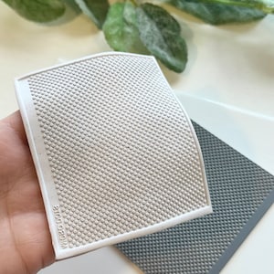 Puede incluir: Dos alfombrillas de silicona blanca y gris con una superficie texturizada de pequeños puntos. Las alfombrillas están etiquetadas como "MICRO DOTS".